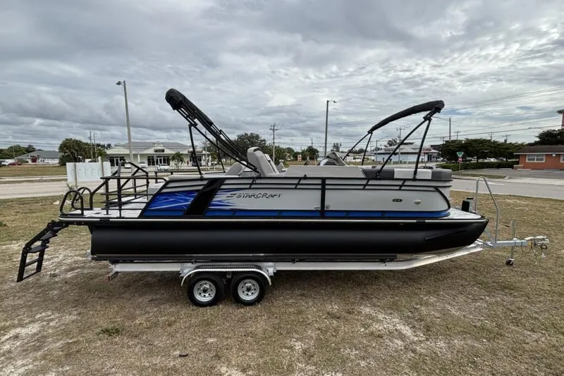 Slide: The Image of 2026 Starcraft SLS 3 Q DH pontoon boat on trailer, parked on grass under cloudy sky. - 4