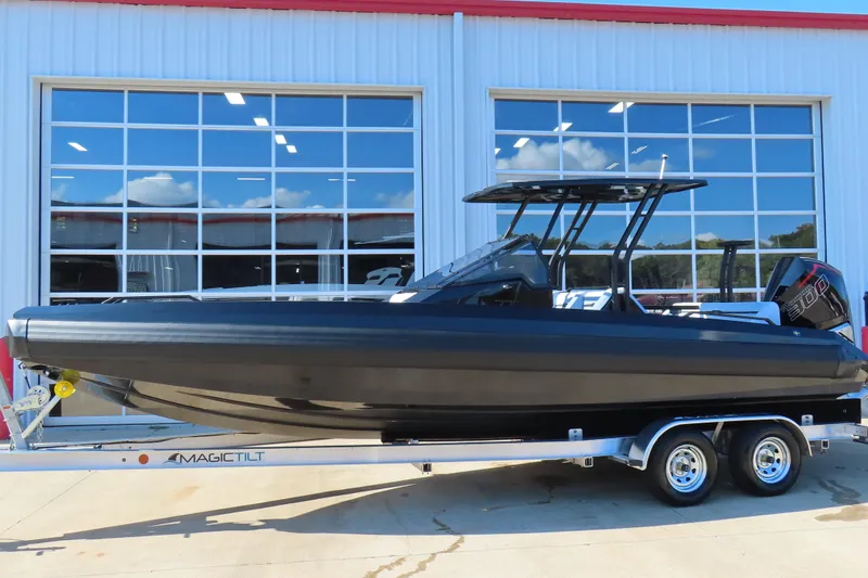 Slide: The Image of 2026 Iron 767 boat on trailer, sleek black design, parked outside a building. - 2