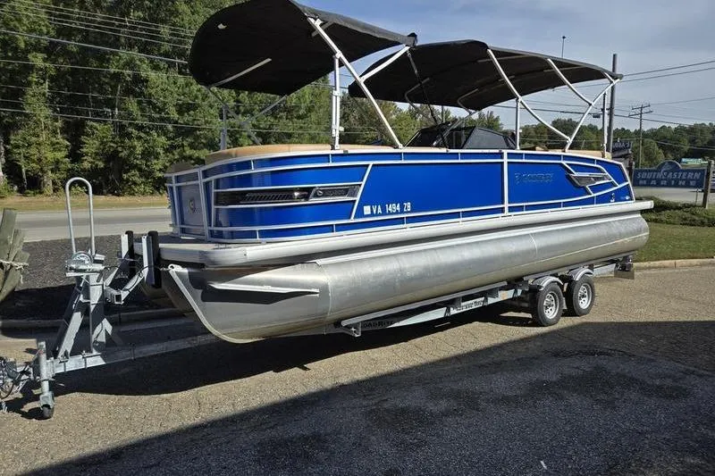 The Image of 2023 Godfrey AquaPatio 255 SBW pontoon boat on trailer, blue exterior, parked outdoors. - 1
