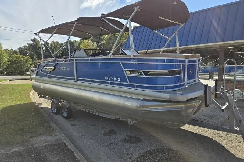Slide: The Image of 2023 Godfrey AquaPatio 255 SBW pontoon boat on trailer, blue exterior, parked outdoors. - 2