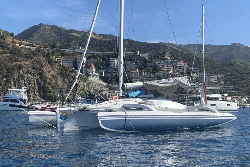 Slide: The Image of 2001 Corsair 31 UC trimaran anchored near scenic coastal town with hills. - 3