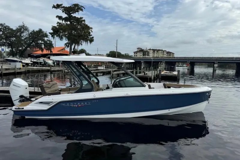 Slide: The Image of 2025 Monterey Elite 27 OB boat docked on a calm waterfront with scenic background. - 24