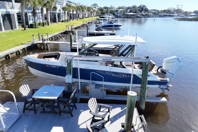 Slide: The Image of 2025 Monterey Elite 27 OB boat docked by waterfront homes, featuring outdoor seating and lush greenery. - 31