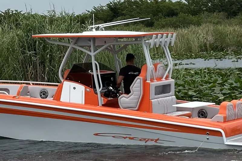 The Image of 2025 Concept 32' CC boat with orange and white design on a lush waterway. - 0