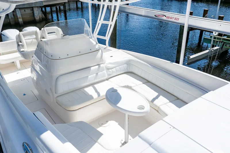 Slide: The Image of 2015 Intrepid 327 Cuddy boat interior with white seating and table, docked by the water. - 27