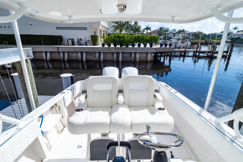 Slide: The Image of 2015 Intrepid 327 Cuddy boat interior with white seating and steering wheel, docked by waterfront homes. - 60