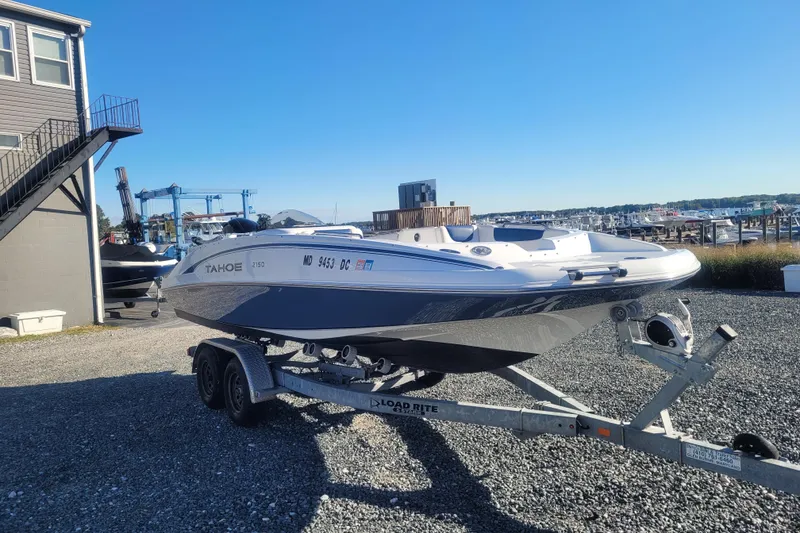 Slide: The Image of 2017 Tahoe 2150 boat on trailer, parked near marina under clear blue sky. - 2