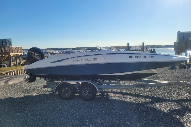 Slide: The Image of 2017 Tahoe 2150 boat on trailer, parked near waterfront, under clear blue sky. - 3
