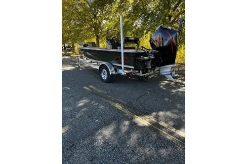 Slide: The Image of 2026 Mako 18 Pro Skiff Backwater Edition boat on trailer, parked under trees. - 2