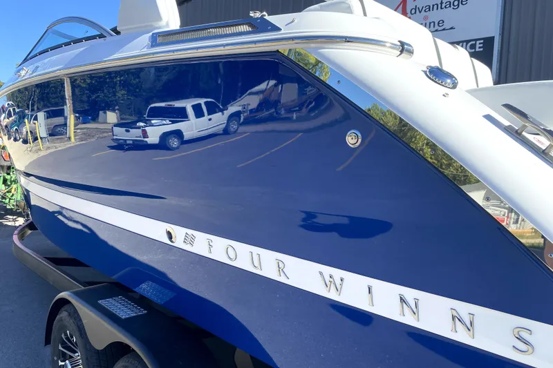 Slide: The Image of 2026 Four Winns H6 boat with sleek blue and white design, parked outdoors. - 3