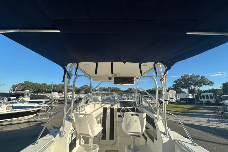 Slide: The Image of 2001 Boston Whaler 23 Conquest boat interior with canopy and seating, docked under clear sky. - 21