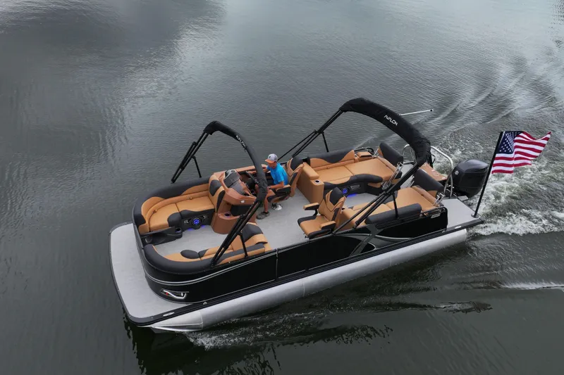 Slide: The Image of 2026 Avalon LSZ Quad Lounger Shift pontoon boat cruising on a lake with American flag. - 2