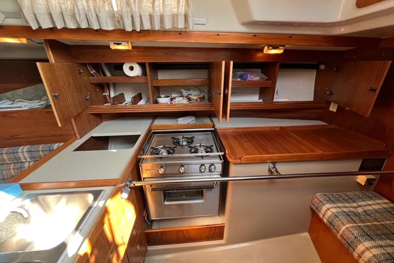 Slide: The Image of 1984 C&C 41 yacht kitchen with stove, wooden cabinets, and plaid seating. - 43