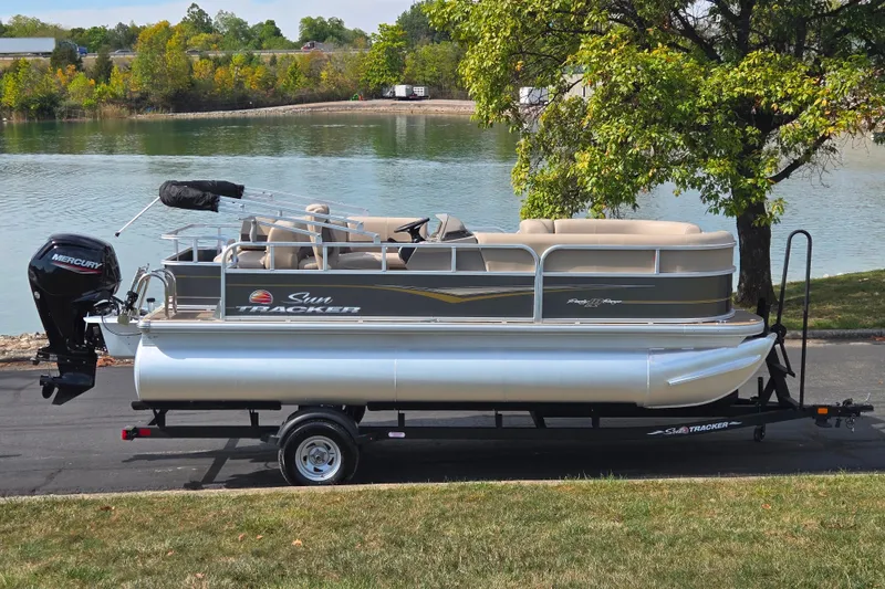 The Image of 2024 Sun Tracker Party Barge 18 DLX pontoon boat on trailer by a lake. - 0