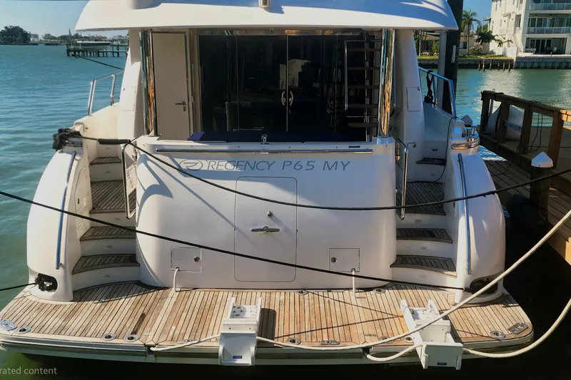 Slide: The Image of 2019 Regency P65 yacht docked, rear view with wooden deck and water backdrop. - 57