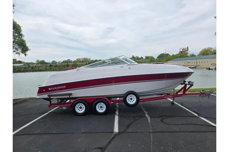 Slide: The Image of 1994 Four Winns 235 Sundowner boat on trailer by a lakeside parking lot. - 9