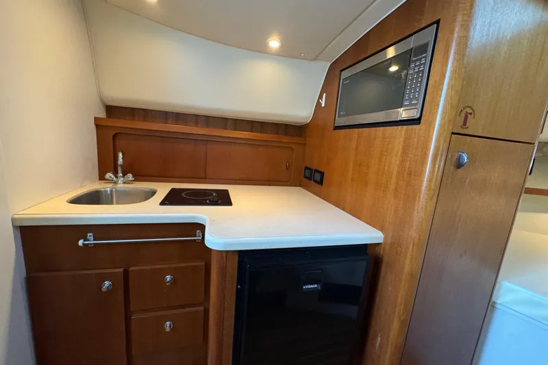 Slide: The Image of 2005 Tiara Yachts 2900 Open galley with sink, stove, microwave, and wood cabinetry. - 12