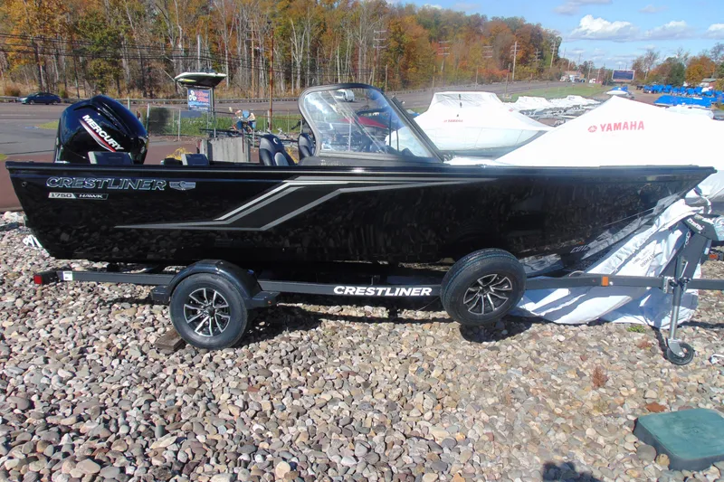 Slide: The Image of 2026 Crestliner 1750 Hawk boat on trailer, black exterior, parked on gravel. - 2