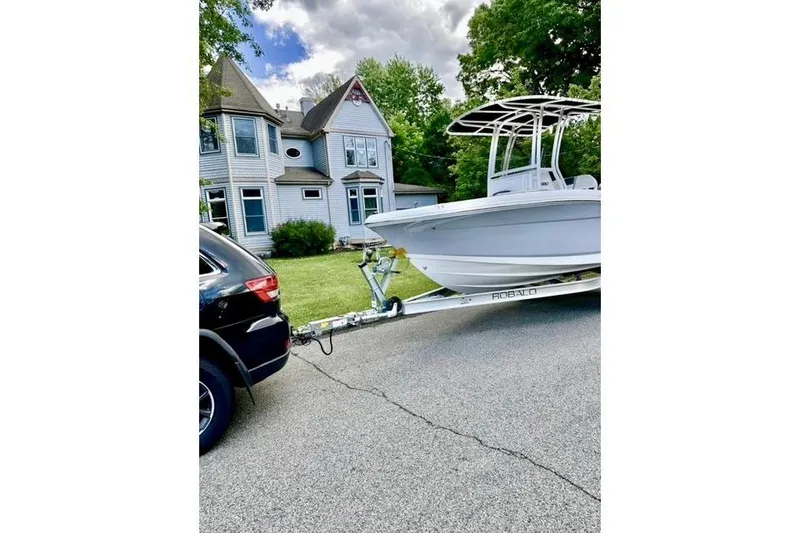Slide: The Image of 2024 Robalo R180 Center Console boat on trailer, parked near a Victorian-style house. - 16
