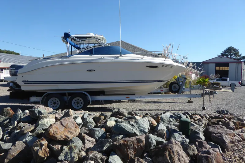The Image of 2004 Sea Ray 225 Weekender boat on trailer, parked outdoors near rocks and buildings. - 0