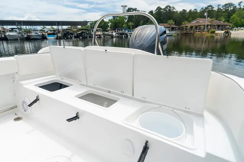 Slide: The Image of 2026 Sea Hunt Ultra 229 boat with open storage compartments, docked by a scenic marina. - 13