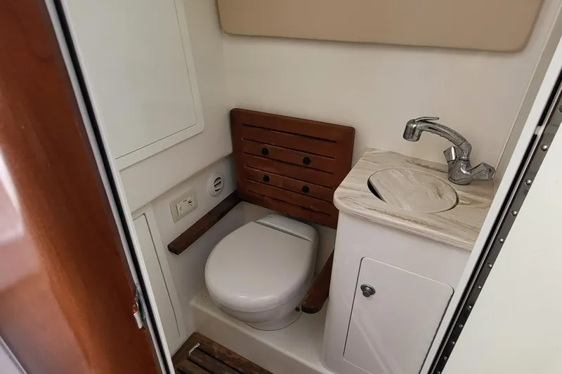 Slide: The Image of 2018 Edgewater 370CC boat bathroom with toilet, sink, and wooden accents. - 10