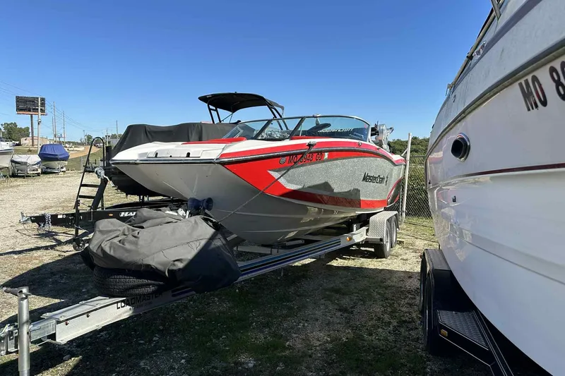 Slide: The Image of 2016 MasterCraft X23 boat on trailer, parked outdoors under clear blue sky. - 7