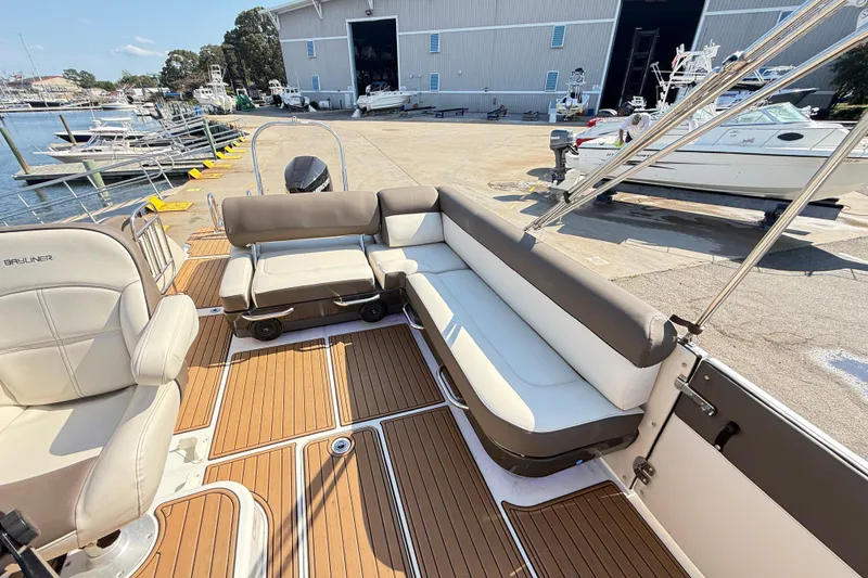 Slide: The Image of 2022 Bayliner Element XR7 boat interior with cushioned seating and wood-style flooring at a marina. - 16