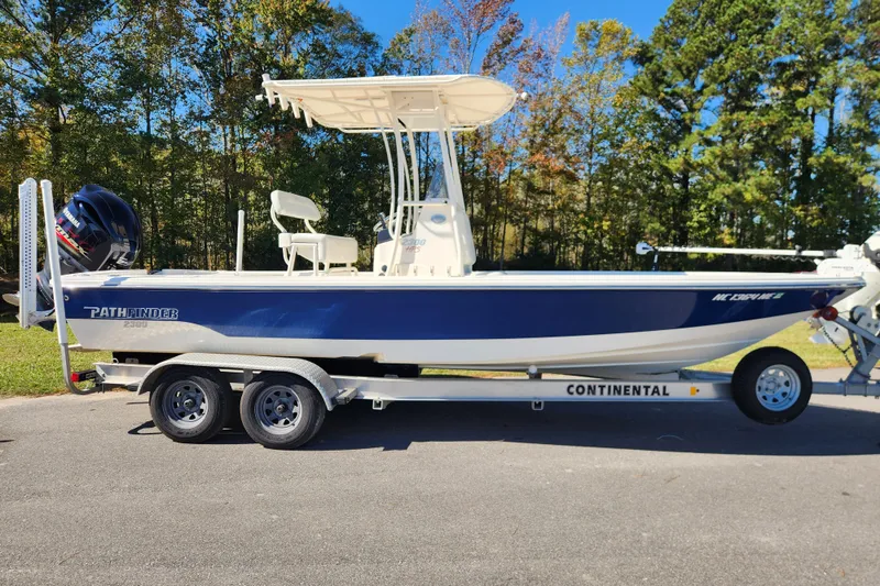 The Image of 2015 Pathfinder 2300 HPS boat on trailer, parked outdoors with trees in background. - 0
