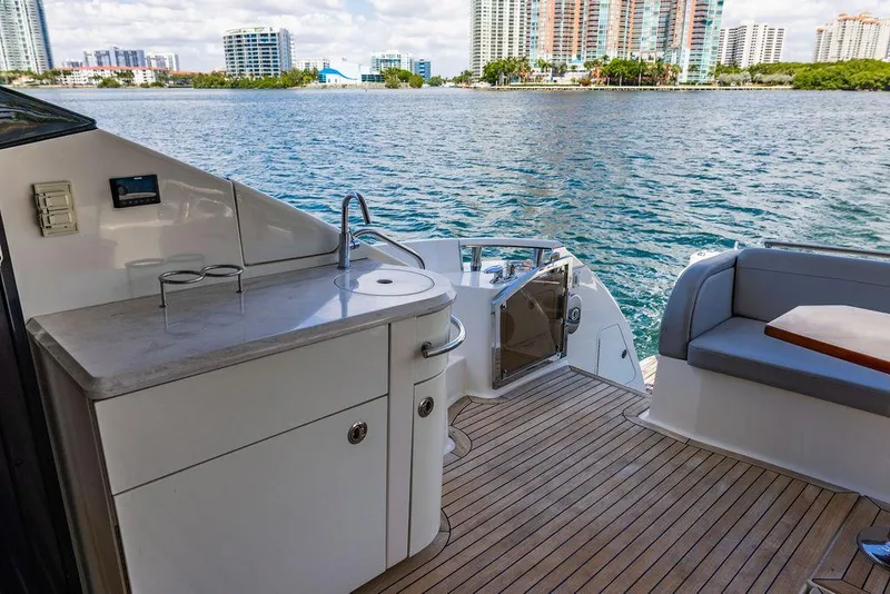 Slide: The Image of 2016 Sea Ray L650 Fly yacht deck with seating and kitchenette, overlooking waterfront cityscape. - 41