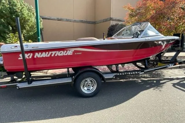 Slide: The Image of 2009 Nautique Ski Nautique 196 boat on trailer, red and black design, parked outdoors. - 0