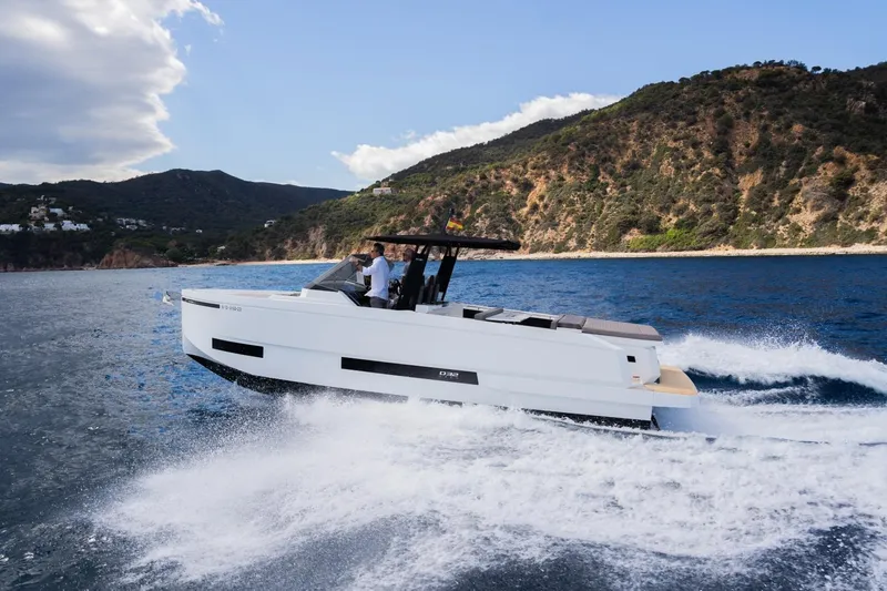 Slide: The Image of 2026 De Antonio Yachts D32 cruising on blue waters near a scenic coastline. - 2