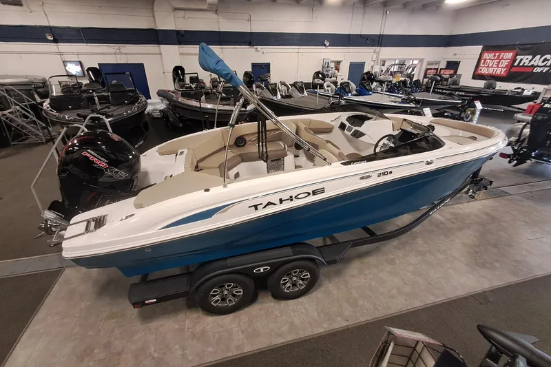 Slide: The Image of 2026 Tahoe 210 S boat displayed indoors on a trailer, surrounded by other boats. - 4