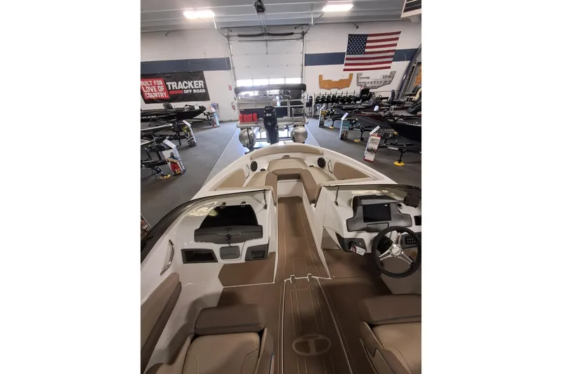 Slide: The Image of 2026 Tahoe 210 S boat interior in showroom with American flag and other boats. - 6