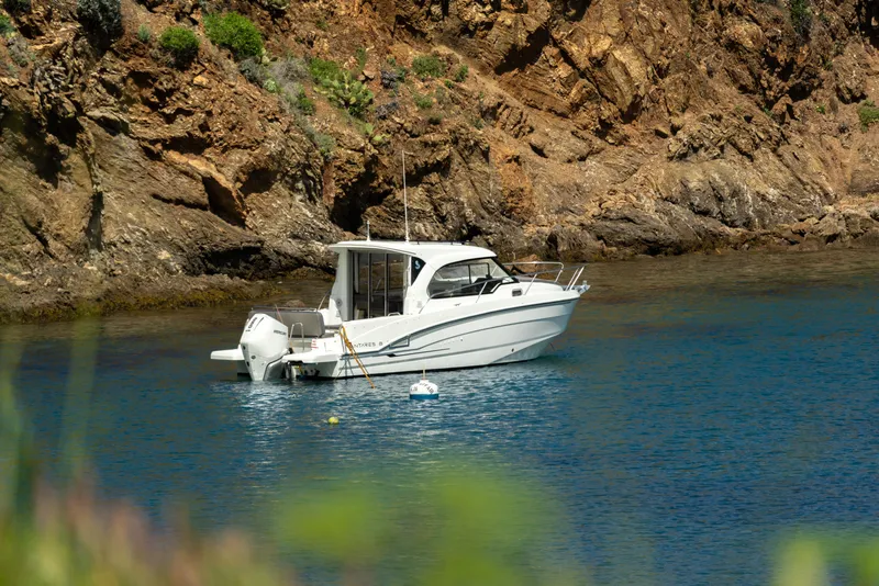 Slide: The Image of 2025 Beneteau Antares 8 boat anchored in a serene rocky cove. - 10