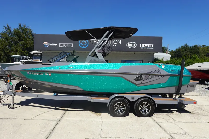 Slide: The Image of 2022 Axis T23 boat with teal and gray design on a trailer at a dealership. - 1