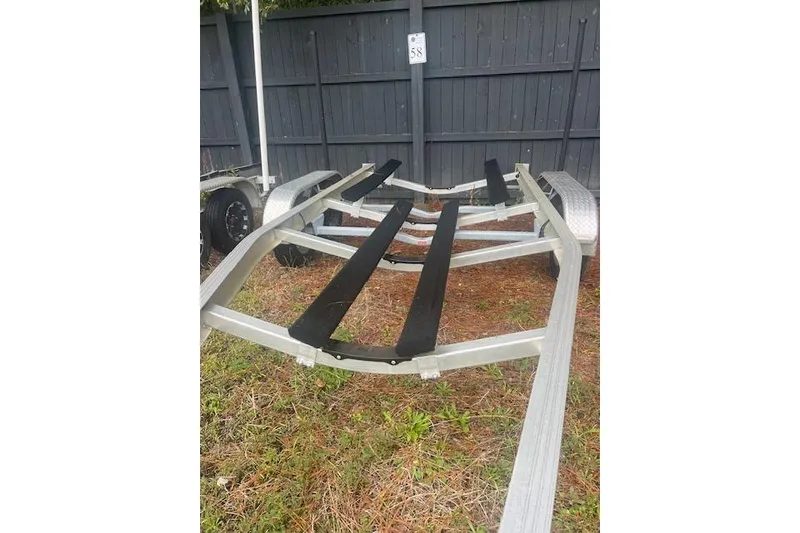 Slide: The Image of Boat trailer for 2022 Chaparral 23 SSi, parked on grass near a wooden fence. - 21