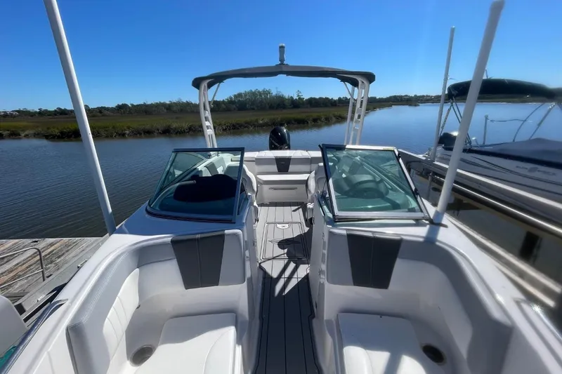 Slide: The Image of 2022 Chaparral 23 SSi boat interior with open cockpit and seating, docked by a serene river. - 6