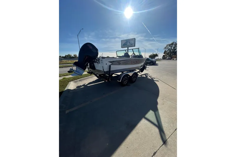 Slide: The Image of 2026 Lund 1875 Impact XS Sport boat on trailer, parked outdoors under clear blue sky. - 16