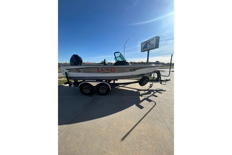 Slide: The Image of 2026 Lund 1875 Impact XS Sport boat with seating and motor, parked near a road. - 18