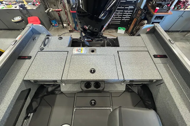 Slide: The Image of 2026 Lund 1875 Impact XS Sport boat interior with storage compartments and motor in a workshop. - 31