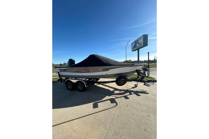 Slide: The Image of 2026 Lund 1875 Impact XS Sport boat on trailer, parked outdoors under clear blue sky. - 9