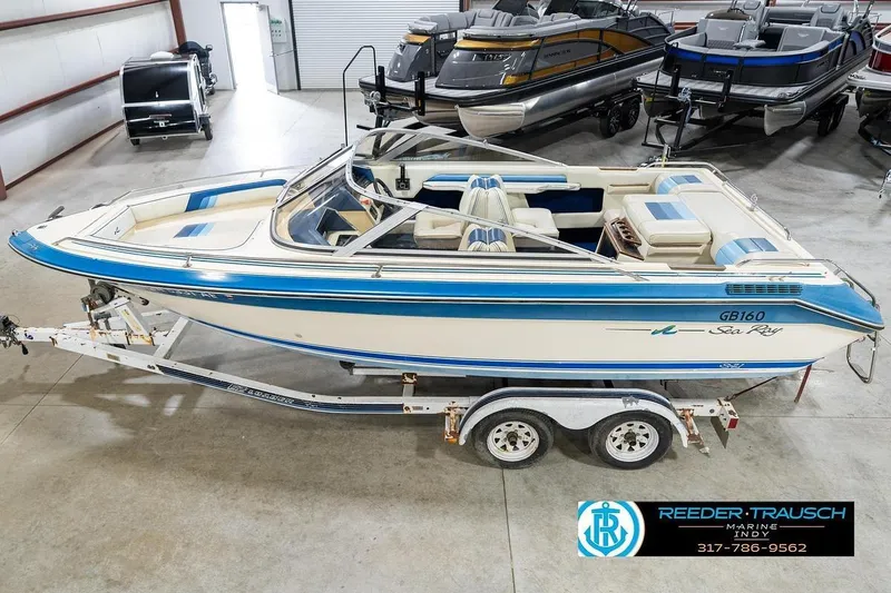 The Image of 1987 Sea Ray Sorrento 21 boat on trailer in showroom, blue and white design. - 2