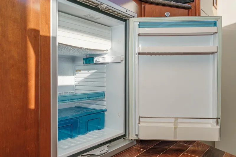 Slide: The Image of Open refrigerator inside 2011 Meridian 341 Sedan yacht, featuring wooden cabinetry and blue-tinted shelves. - 30
