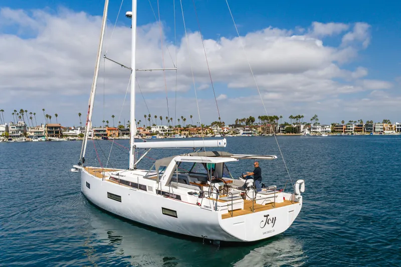 Slide: The Image of 2023 Beneteau Oceanis Yacht 60 sailing near coastal homes under blue skies. - 2