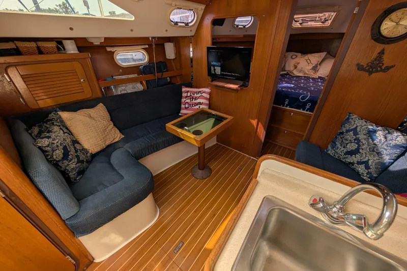 Slide: The Image of 2004 Catalina 310 yacht interior with cozy seating, wooden finishes, and a compact kitchen area. - 2