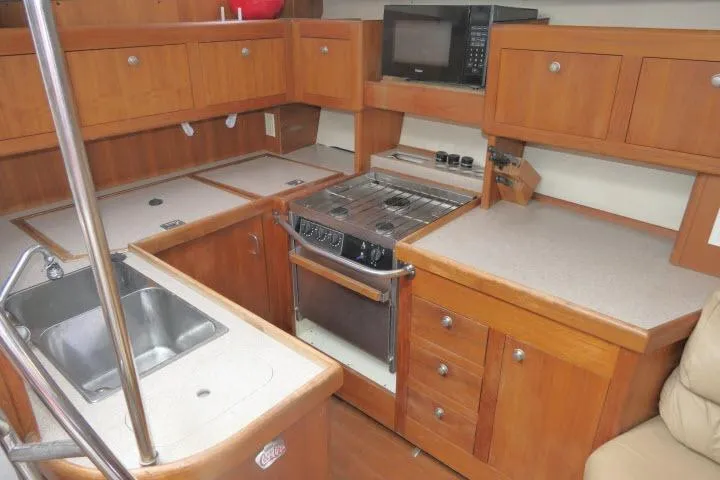 Slide: The Image of 1999 Hunter 450 Passage yacht kitchen with wooden cabinets, stove, sink, and microwave. - 13