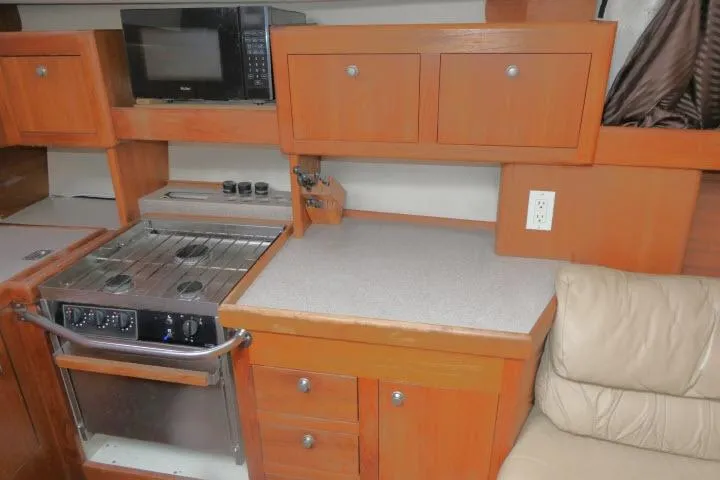 Slide: The Image of 1999 Hunter 450 Passage yacht kitchen with stove, microwave, and wooden cabinetry. - 19