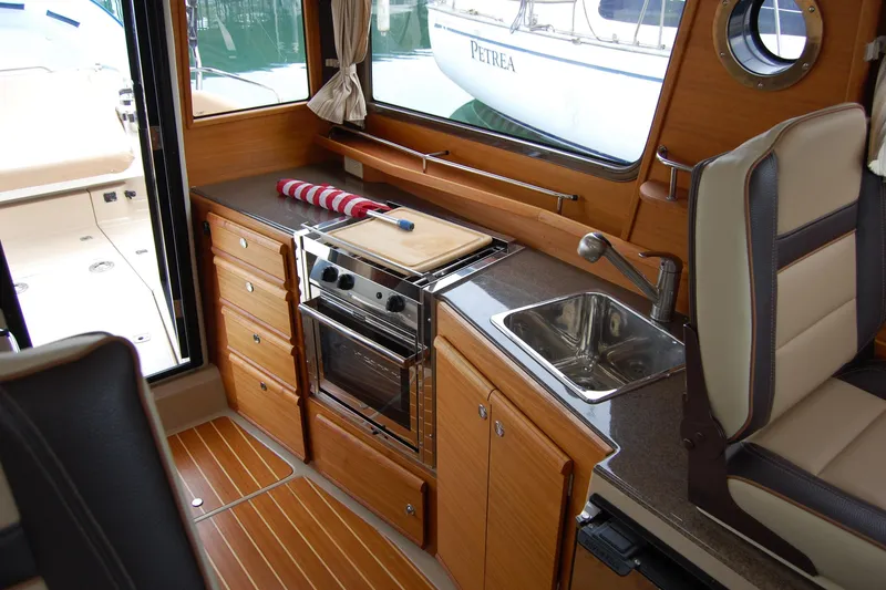 Slide: The Image of 2018 Ranger Tugs R29 interior kitchen with stove, sink, and wooden cabinetry. - 27
