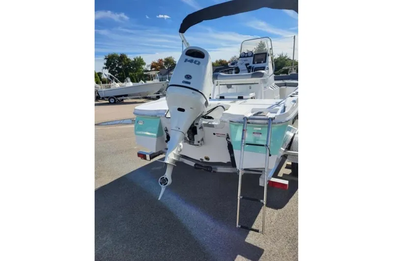 Slide: The Image of 2025 NauticStar 191 Hybrid boat with outboard motor and ladder, parked outdoors. - 7